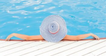 Frau von Hinten mit seitlich ausgestreckten Armen und Sonnenhut im Pool